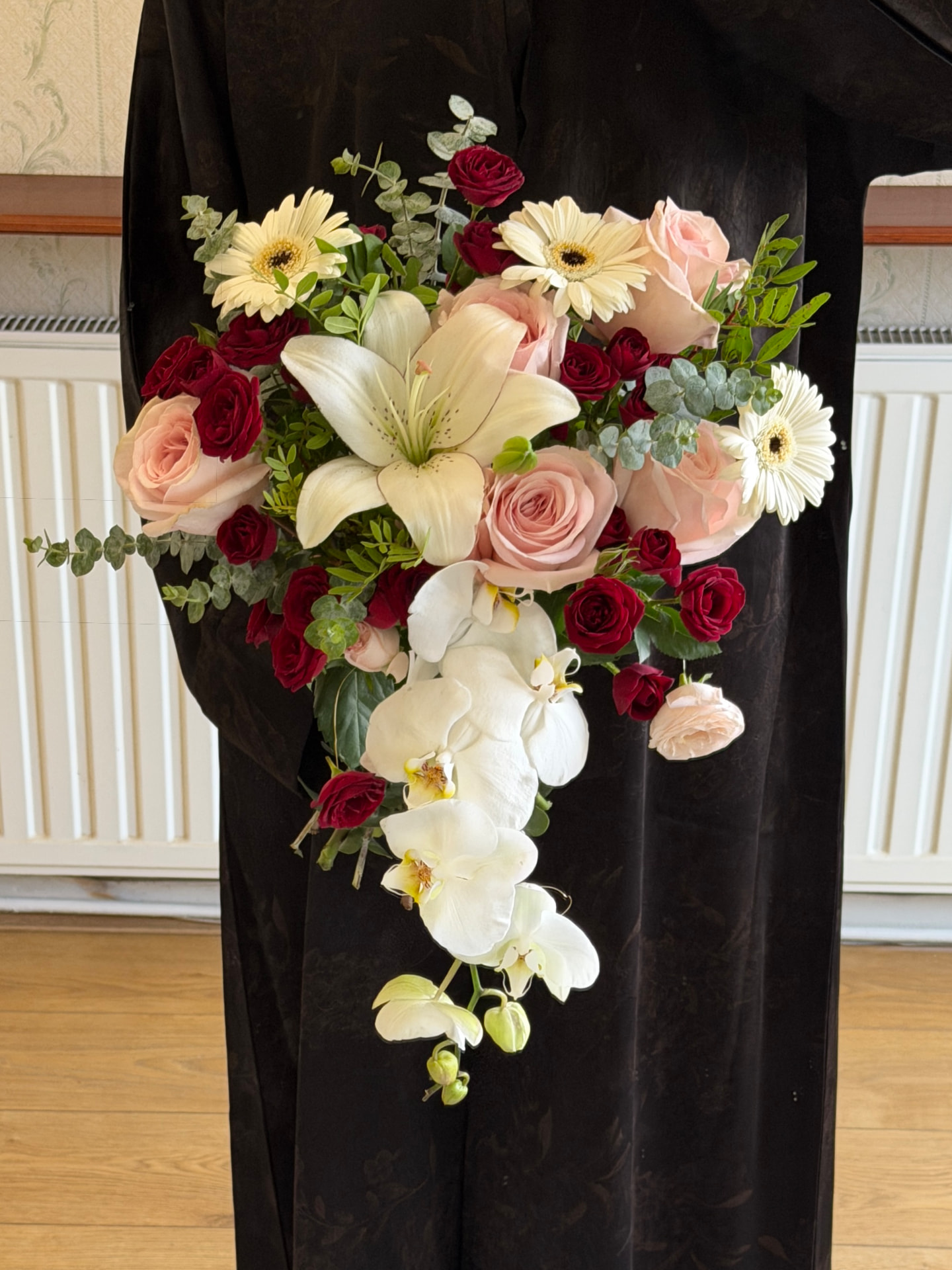 A cascading bridal bouquet of blush and burgundy roses, white lilies, orchids and gerbera daisies.